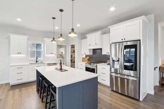 kitchen featuring appliances with stainless steel finishes, wood finished floors, a center island, light countertops, and a sink