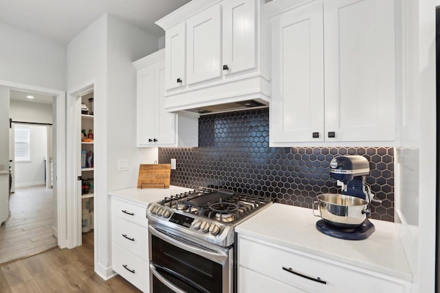 kitchen with a barn door, range with two ovens, light wood-type flooring, white cabinetry, and backsplash