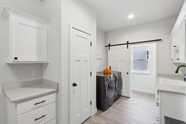 laundry room with a barn door, a sink, light wood-type flooring, independent washer and dryer, and baseboards