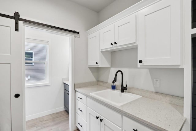 kitchen with a barn door, a sink, white cabinetry, baseboards, and light wood-type flooring