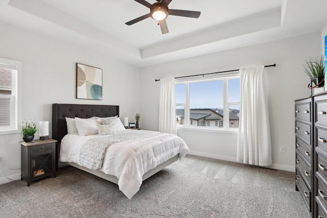 carpeted bedroom featuring ceiling fan, a tray ceiling, and baseboards