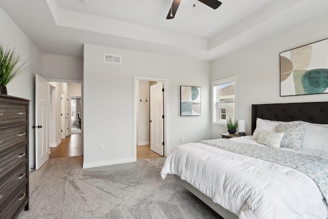 bedroom with light carpet, visible vents, a tray ceiling, and baseboards