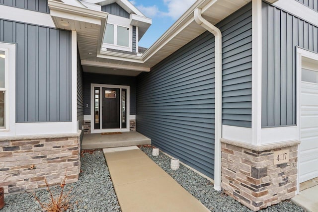 doorway to property featuring an attached garage, stone siding, and board and batten siding