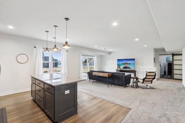 kitchen with a barn door, light wood-style flooring, light stone counters, pendant lighting, and recessed lighting