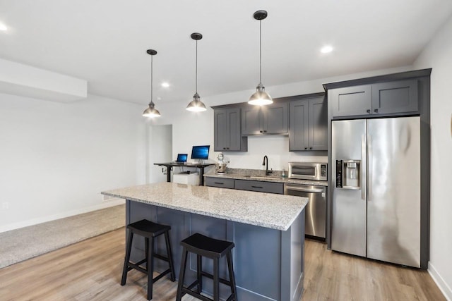 kitchen with a center island, a breakfast bar area, appliances with stainless steel finishes, a sink, and light stone countertops