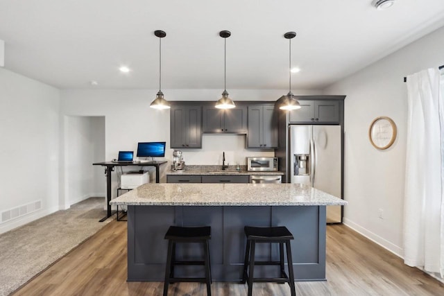 kitchen with a sink, visible vents, appliances with stainless steel finishes, a center island, and a kitchen bar