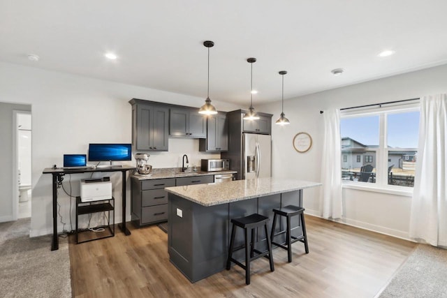 kitchen featuring a breakfast bar, decorative light fixtures, appliances with stainless steel finishes, a kitchen island, and light stone countertops