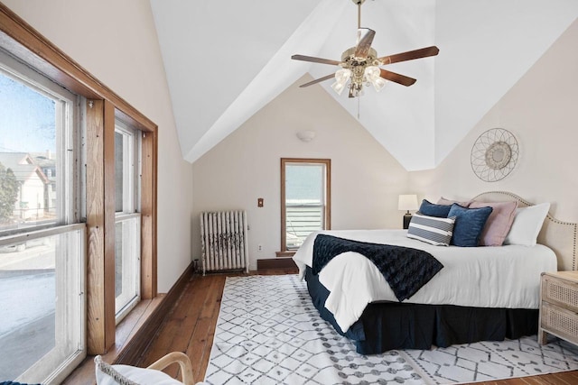 bedroom featuring vaulted ceiling, radiator heating unit, multiple windows, and wood-type flooring