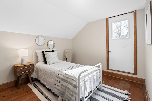 bedroom featuring lofted ceiling, radiator, baseboards, and hardwood / wood-style flooring