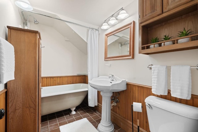 full bath with a soaking tub, toilet, wainscoting, wooden walls, and tile patterned floors