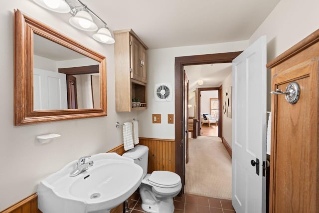 half bathroom featuring tile patterned flooring, wooden walls, a sink, visible vents, and wainscoting