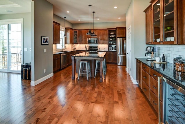 kitchen with a kitchen island, glass insert cabinets, appliances with stainless steel finishes, dark stone countertops, and hanging light fixtures