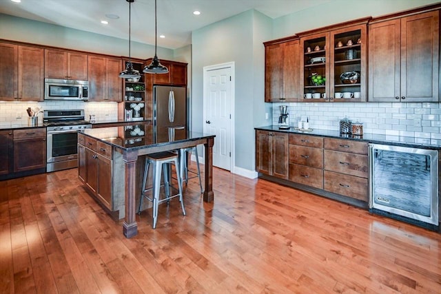 kitchen featuring beverage cooler, dark stone counters, a kitchen island, hanging light fixtures, and stainless steel appliances