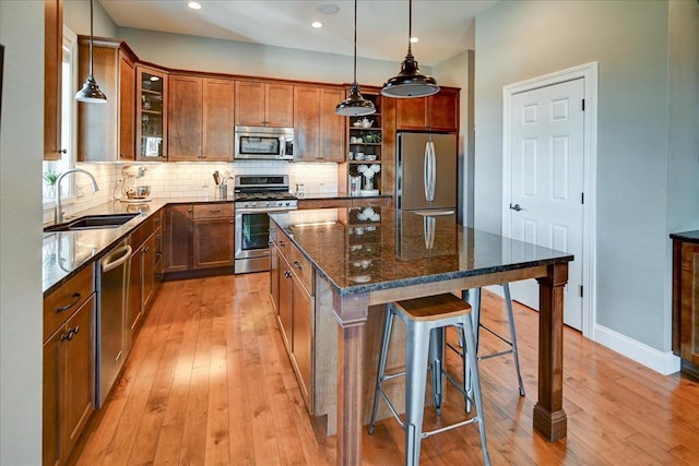 kitchen featuring a center island, stainless steel appliances, glass insert cabinets, a sink, and dark stone countertops