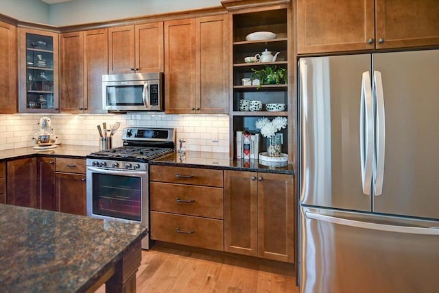 kitchen with stainless steel appliances, light wood-type flooring, dark stone countertops, and brown cabinets