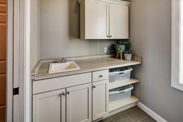 kitchen featuring baseboards, light countertops, a sink, and white cabinets