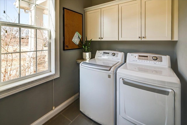 clothes washing area with dark tile patterned flooring, washing machine and dryer, cabinet space, and baseboards