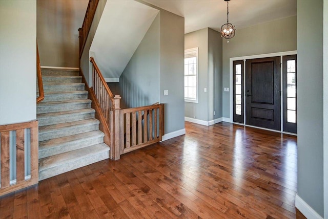 foyer entrance with a notable chandelier, dark wood-style flooring, stairs, and baseboards