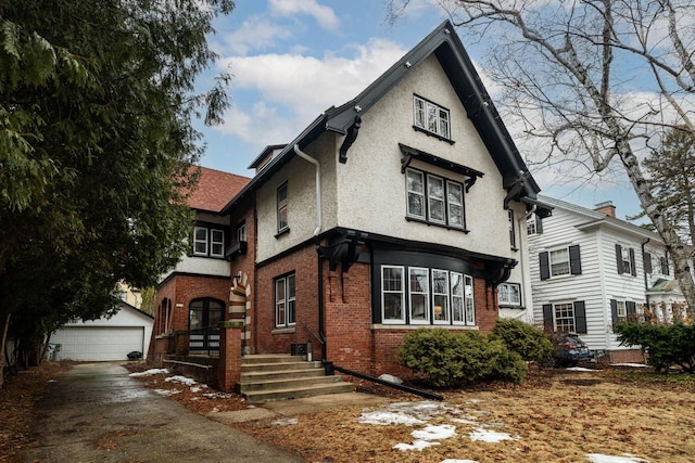 english style home with a garage, an outbuilding, brick siding, and stucco siding