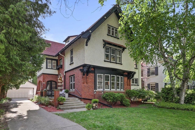 view of front of house with an outbuilding, brick siding, a detached garage, stucco siding, and a front yard