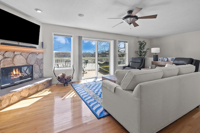 living room featuring a stone fireplace, wood finished floors, and a ceiling fan