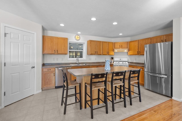 kitchen with a breakfast bar area, under cabinet range hood, a sink, a kitchen island, and appliances with stainless steel finishes