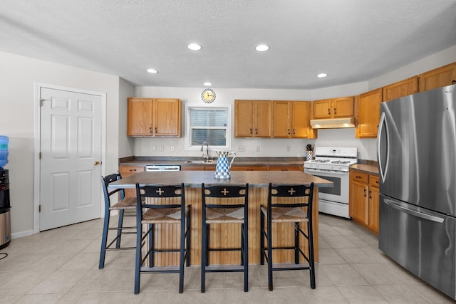 kitchen featuring dark countertops, a kitchen island, freestanding refrigerator, under cabinet range hood, and gas range gas stove