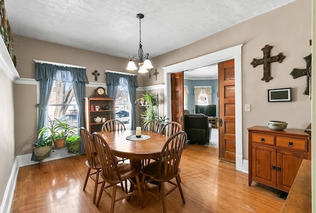 dining room with light wood-style flooring, a textured ceiling, baseboards, and a notable chandelier