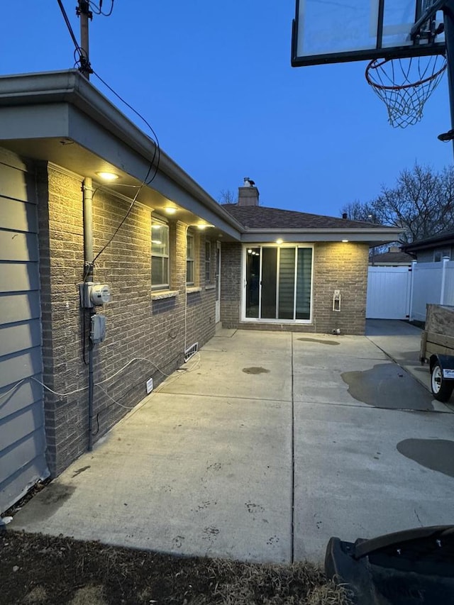 back of house at dusk with a patio area, fence, and brick siding