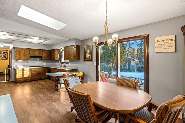 dining area featuring a skylight, a notable chandelier, a textured ceiling, and dark wood-type flooring