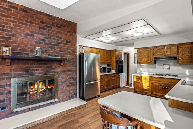 kitchen with a fireplace, wood finished floors, light countertops, appliances with stainless steel finishes, and brown cabinetry