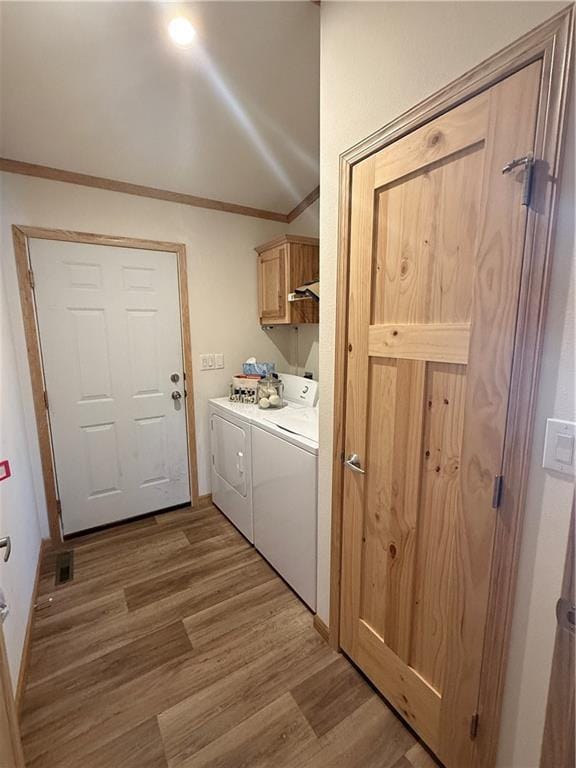 clothes washing area with cabinet space, ornamental molding, washer and dryer, and wood finished floors