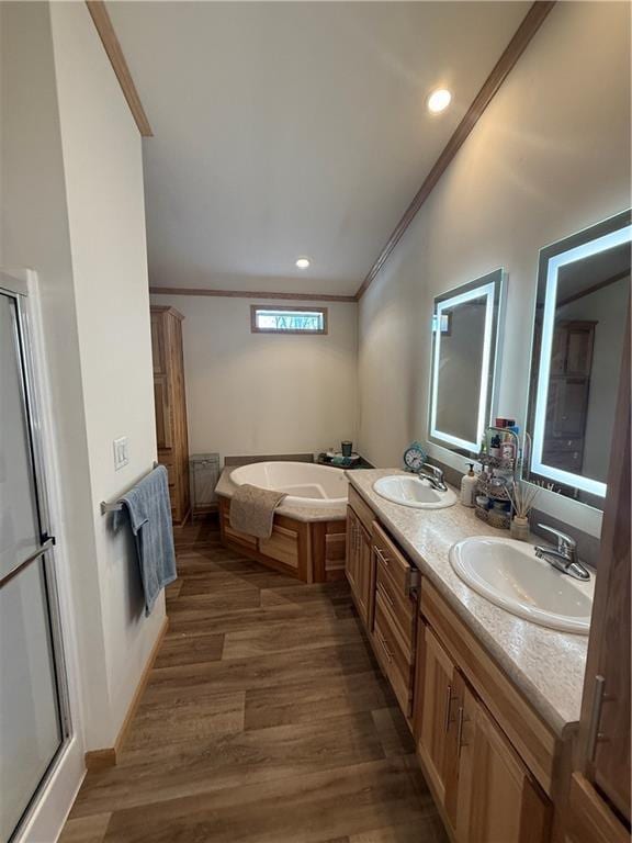 bathroom with crown molding, a garden tub, a sink, and wood finished floors