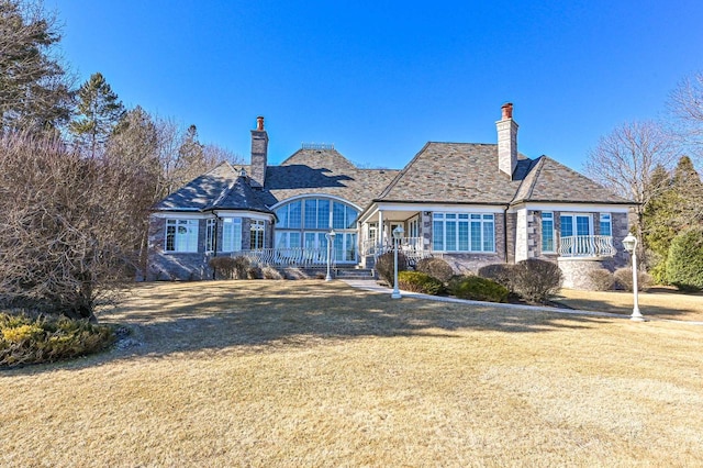 view of front of home with a high end roof, a porch, a chimney, and a front lawn