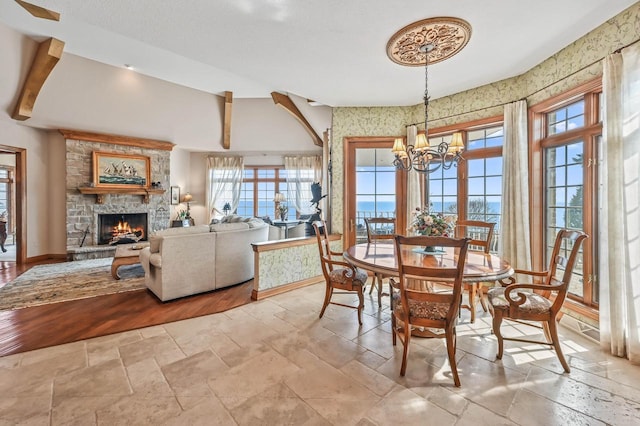 dining room with a stone fireplace, an inviting chandelier, stone tile floors, and baseboards