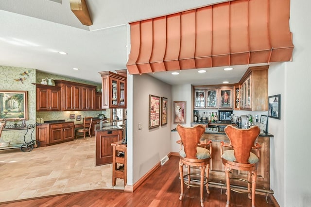 kitchen featuring visible vents, light wood-style floors, brown cabinetry, glass insert cabinets, and baseboards