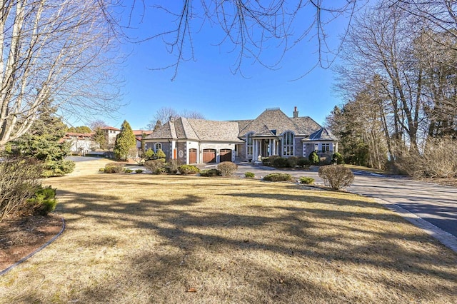 view of front facade with stone siding, a front yard, and a chimney