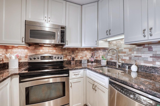 kitchen featuring appliances with stainless steel finishes, dark stone counters, white cabinetry, and a sink