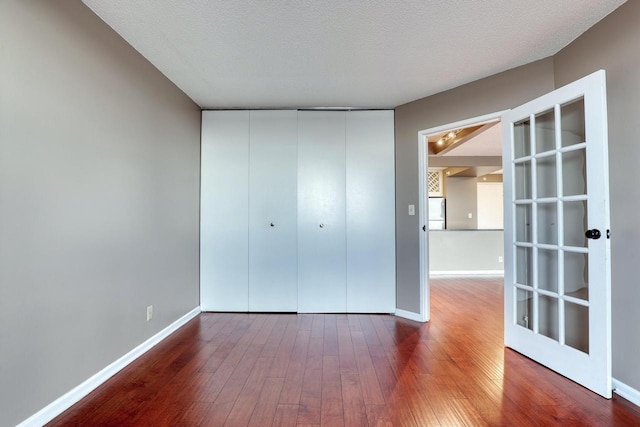 unfurnished bedroom featuring a textured ceiling, hardwood / wood-style floors, a closet, and baseboards