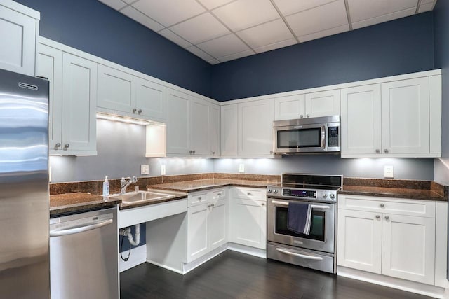 kitchen with dark stone counters, stainless steel appliances, a drop ceiling, and white cabinets