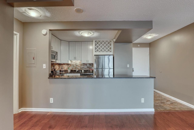 kitchen featuring dark stone counters, appliances with stainless steel finishes, a peninsula, white cabinetry, and backsplash