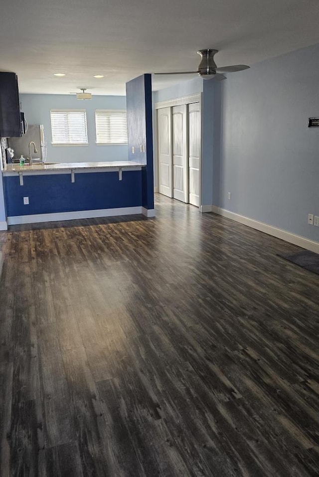 unfurnished living room featuring baseboards and dark wood-style flooring