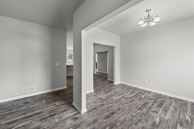 spare room featuring dark wood-style flooring, visible vents, baseboards, and an inviting chandelier