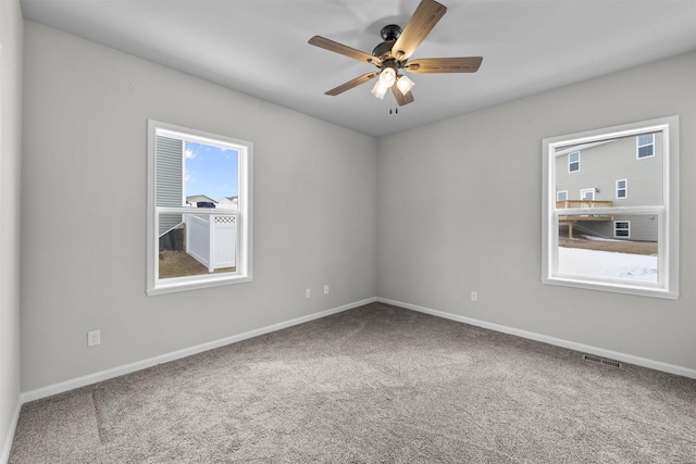 carpeted spare room with baseboards, a ceiling fan, visible vents, and a healthy amount of sunlight