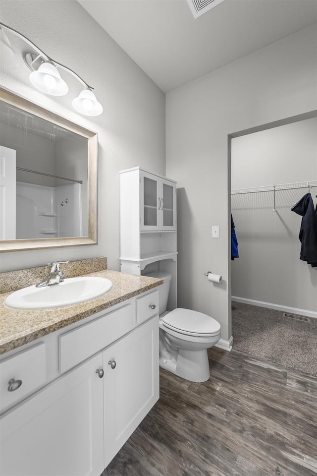 bathroom with wood finished floors, vanity, baseboards, a walk in closet, and walk in shower