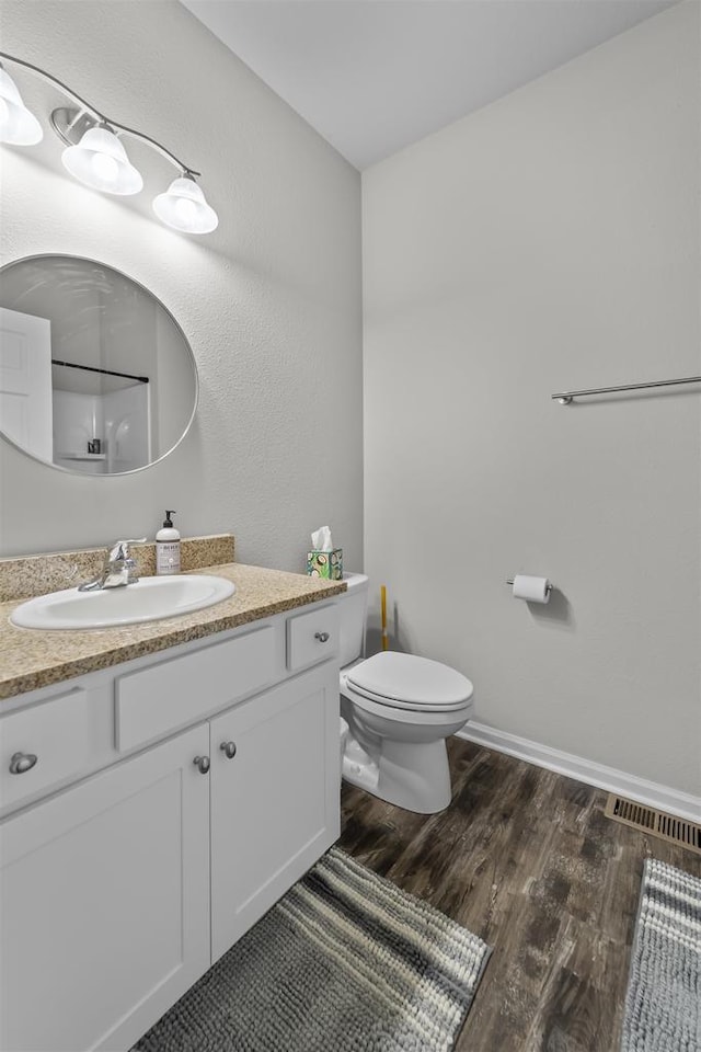 bathroom featuring visible vents, baseboards, toilet, wood finished floors, and vanity