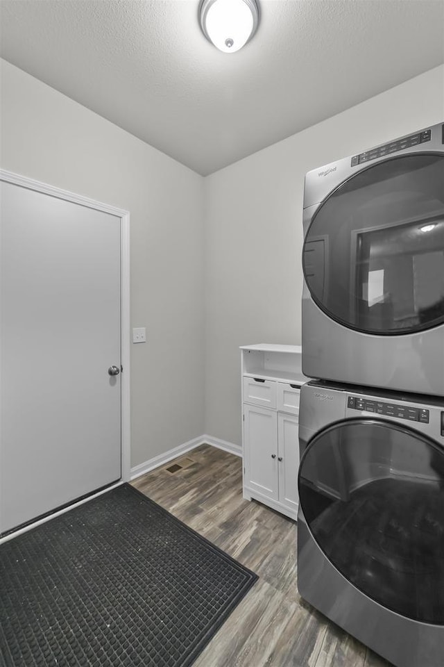 laundry room featuring a textured ceiling, light wood-style flooring, stacked washer and dryer, baseboards, and cabinet space