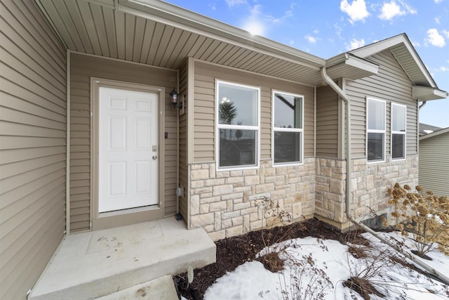 snow covered property entrance with stone siding