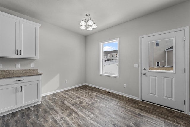 unfurnished dining area featuring dark wood-style floors, a chandelier, and baseboards