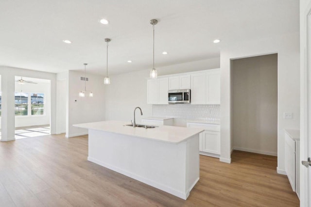 kitchen featuring light countertops, stainless steel microwave, a sink, and white cabinetry